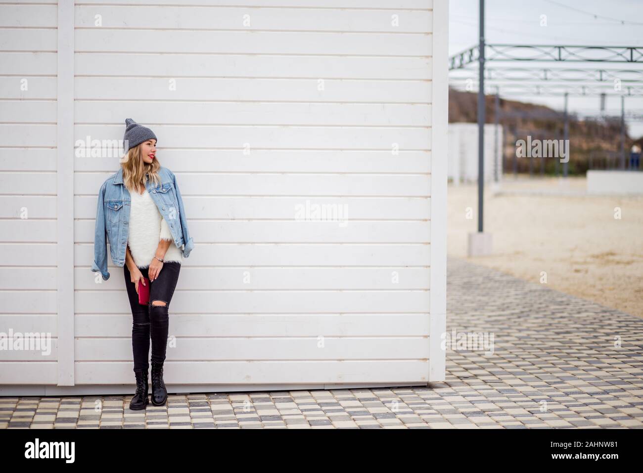 La donna in bianco maglione e camicia di jeans con smartphote staninh  contro bianco parete in legno. Look alla moda abbigliamento o winter in  Europa Foto stock - Alamy