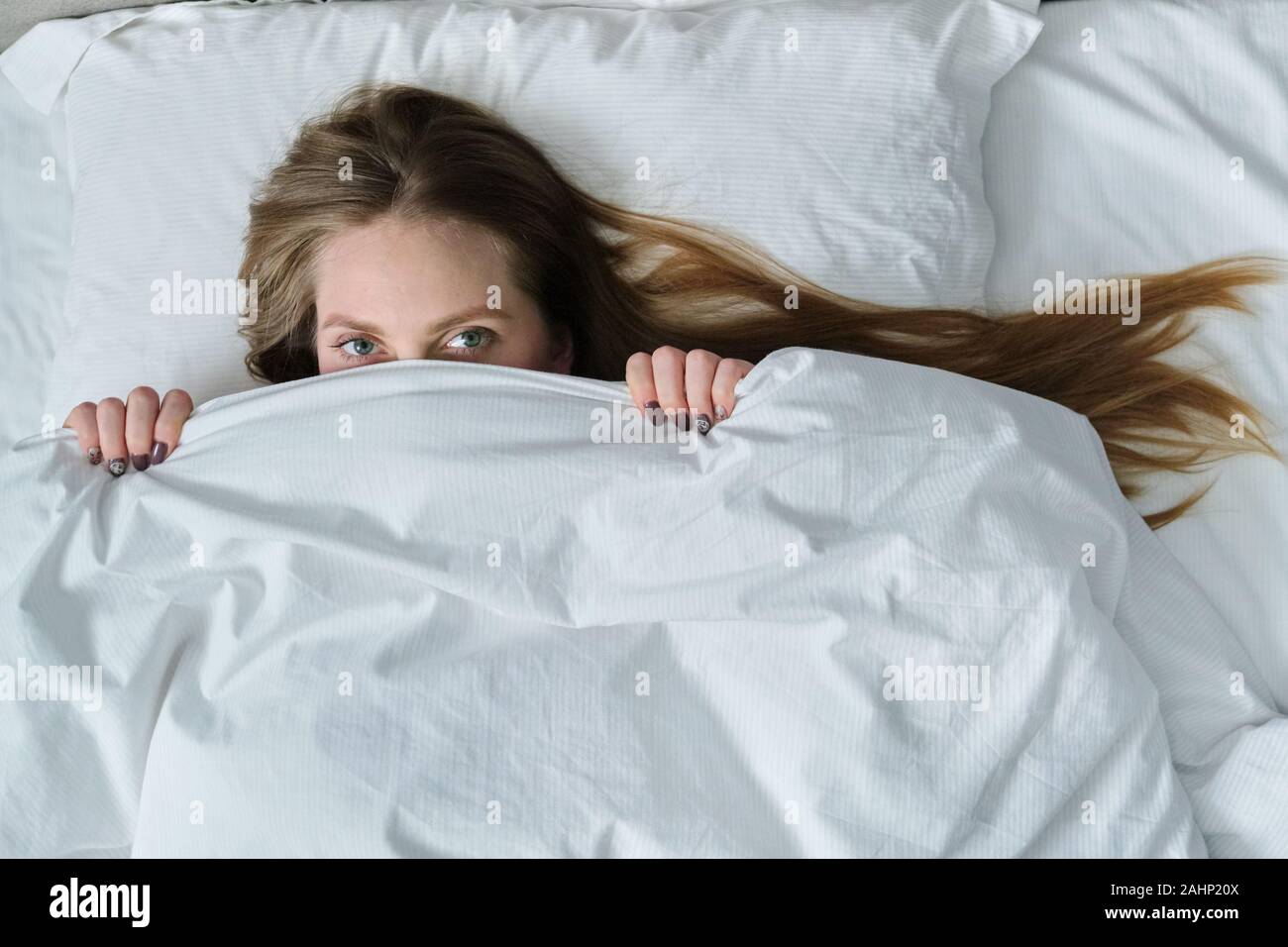 Volto del giovane bella donna giaceva sul cuscino nel letto con coperta,  ponendo ragazza sorridente che copre il volto, vista dall'alto Foto stock -  Alamy