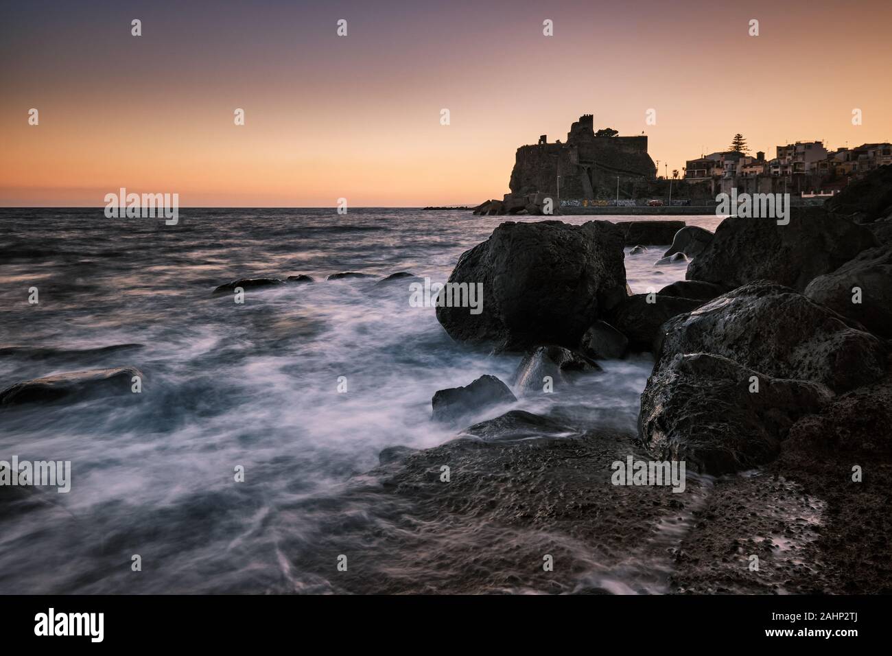 Tramonto su Aci Castello con onde che si infrangono sulle rocce in primo piano, Catania, Italia Foto Stock