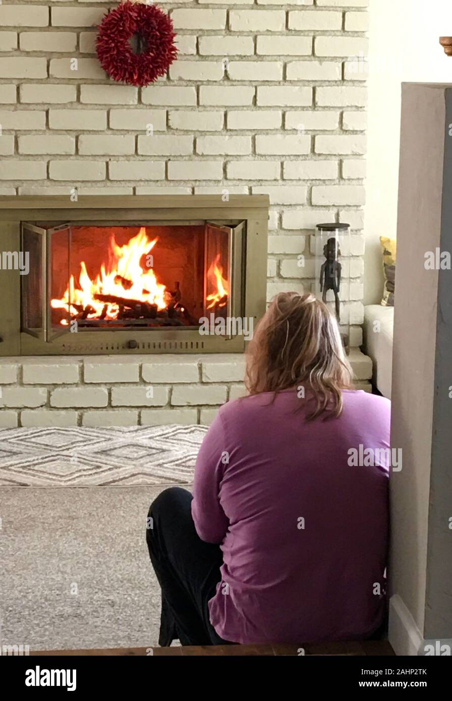 Donna seduta davanti al camino con uno scoppiettante fuoco di legna su un  inverno di mattina Foto stock - Alamy