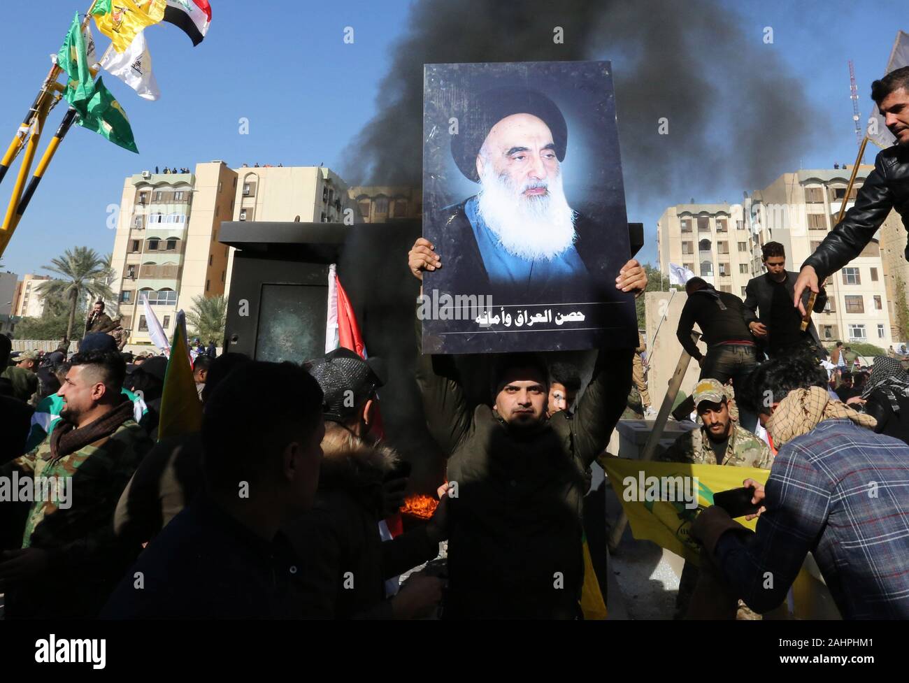 Baghdad in Iraq. 31 Dic, 2019. Un iracheno sostenitore di hashing al-Shaabi rete militare solleva un'immagine dell'Iraq la cima del chierico sciita il grande ayatollah Ali Sistani durante un rally di fronte all'AMBASCIATA DEGLI STATI UNITI nella capitale Baghdad, Iraq, Martedì, Dicembre. 31, 2019. Decine di angry sciita irachena i sostenitori della milizia si rompe in Stati Uniti Composto di ambasciata a Baghdad il martedì dopo lo sfondamento di una porta principale e l'impostazione di fuoco ad un area di ricevimento, prompting gas lacrimogeni e suoni di cannonate. Testimoni ha detto. Foto di Humam Mohamed /UPI Credito: UPI/Alamy Live News Foto Stock