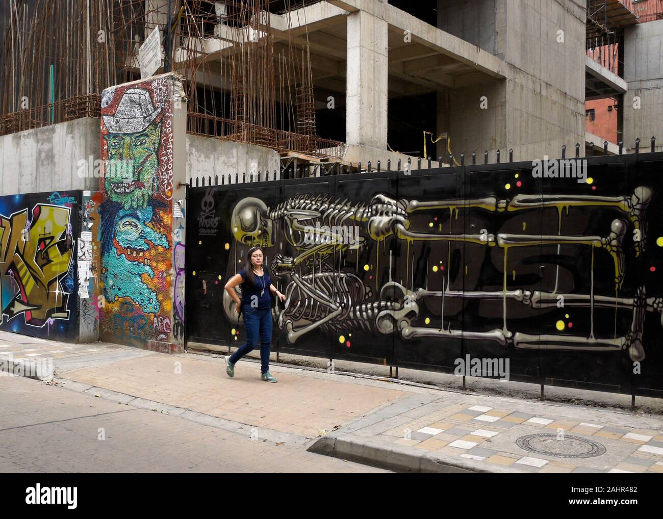 Donna oltrepassando la street art e graffiti dipinta sul gate e l'esterno del palazzo in costruzione in Candelaria distretto di Bogotà, Colombia Foto Stock