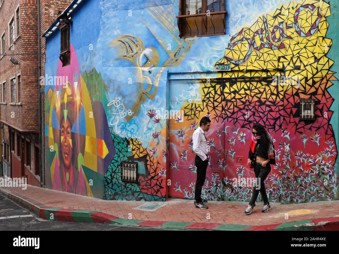 Coppia in angolo di strada con murales e graffiti dipinti su esterno dell edificio in Candelaria distretto di Bogotà, Colombia Foto Stock