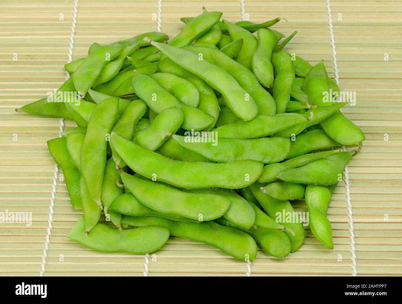 Pila di edamame bolliti, verde fagioli di soia, maodou, su di un tappeto di bambù. In acqua salata cuocere i fagioli di soia, Glycine max, un ricco di proteine legume. Foto Stock