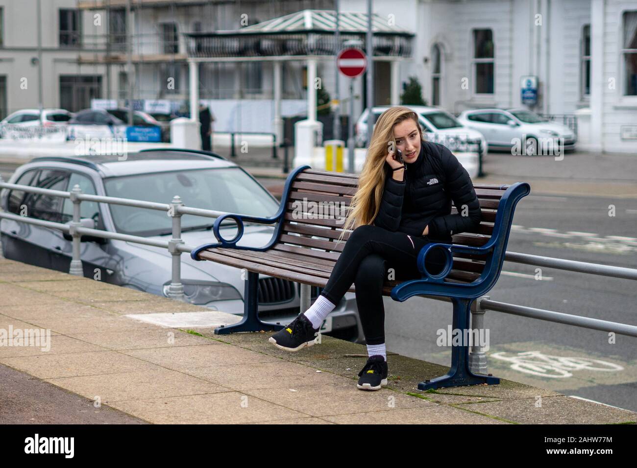 Una ragazza adolescente in sportswear seduta su una panchina in strada a parlare sul suo telefono cellulare o telefono cellulare Foto Stock