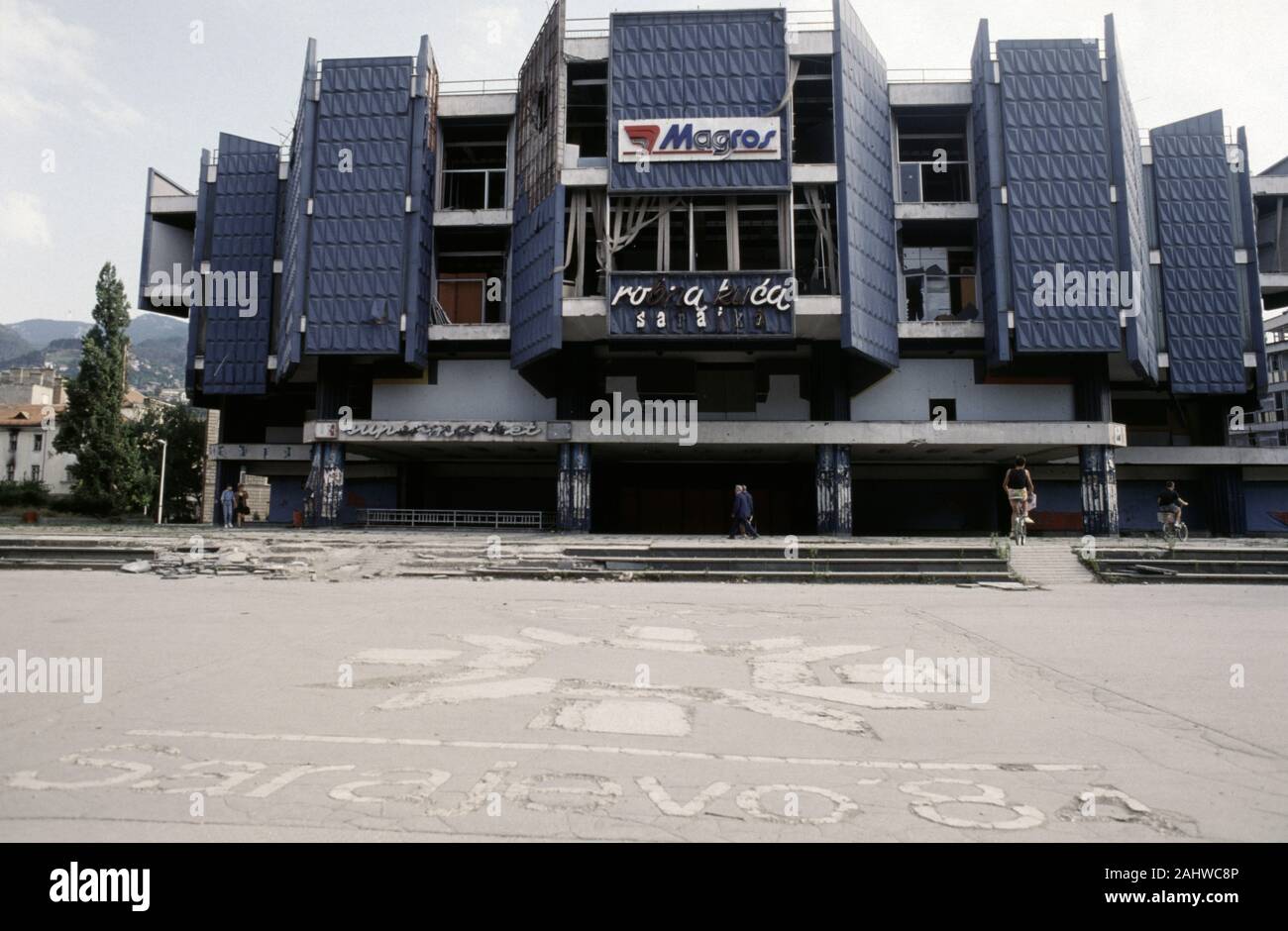 Il 17 agosto 1993 durante l'assedio di Sarajevo: un guscio-danneggiato department store sorge oltre il simbolo usurati per i Giochi Olimpici Invernali del 1984, costruito nella pavimentazione dei figli di Sarajevo Square nel centro della citta'. Foto Stock