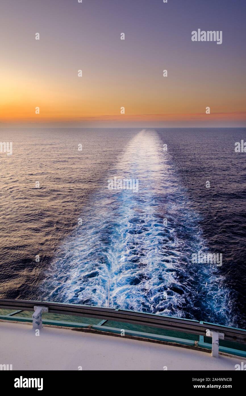 Un colpo delle navi sveglia preso dalla parte posteriore o poppa di una nave mentre si vendita attraverso il mare al tramonto. Foto Stock
