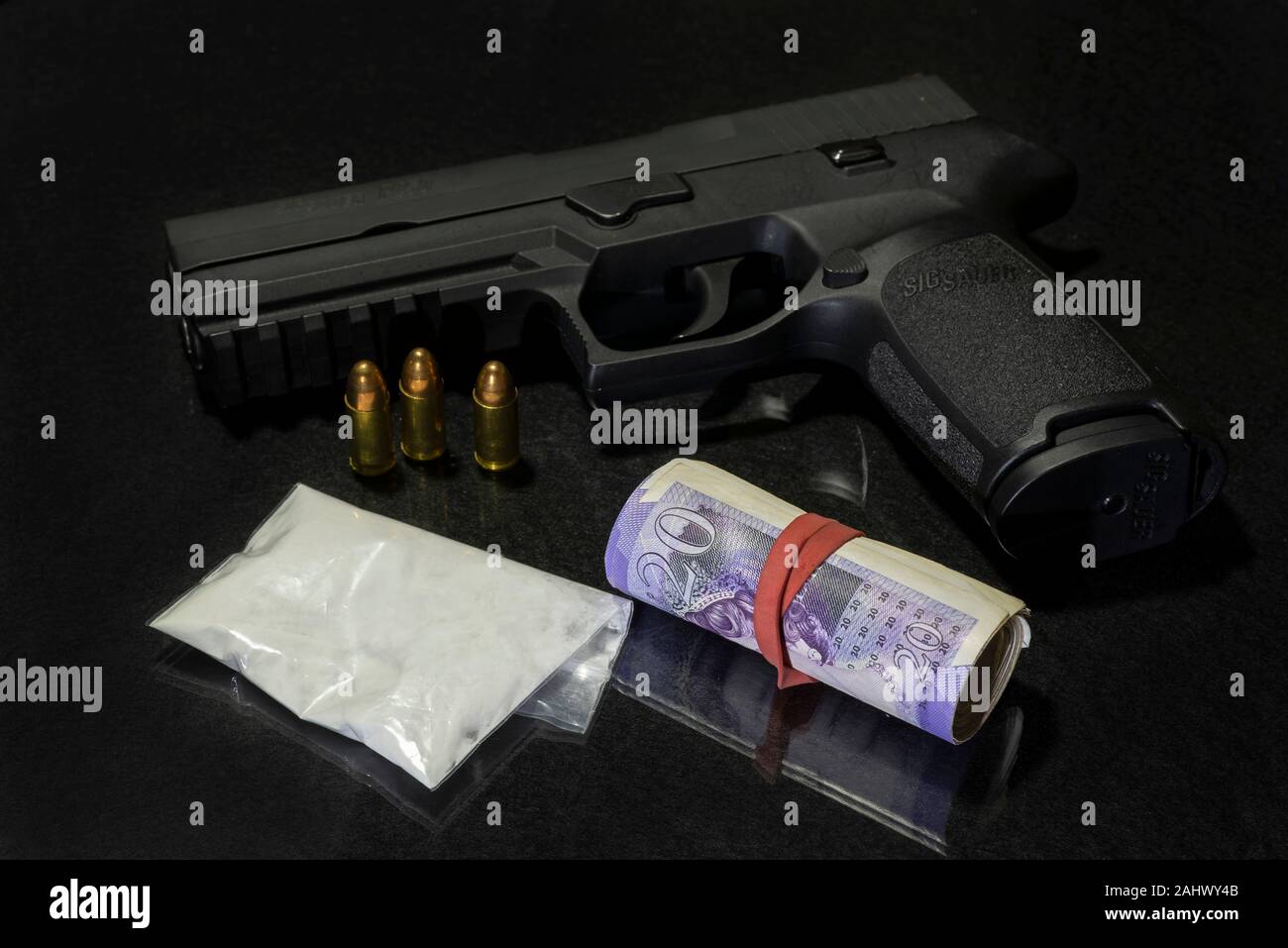 Sacchetto di farmaci in polvere con una Sig Sauer pistola e un rotolo di £20 pound note (GBP) su uno sfondo nero. Foto Stock