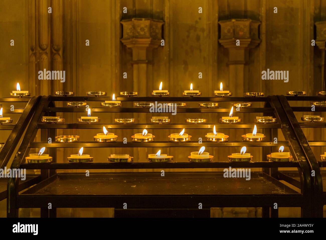 Una candela votiva rack o il cero della preghiera rack con righe di sfarfallio candele accese. Foto Stock