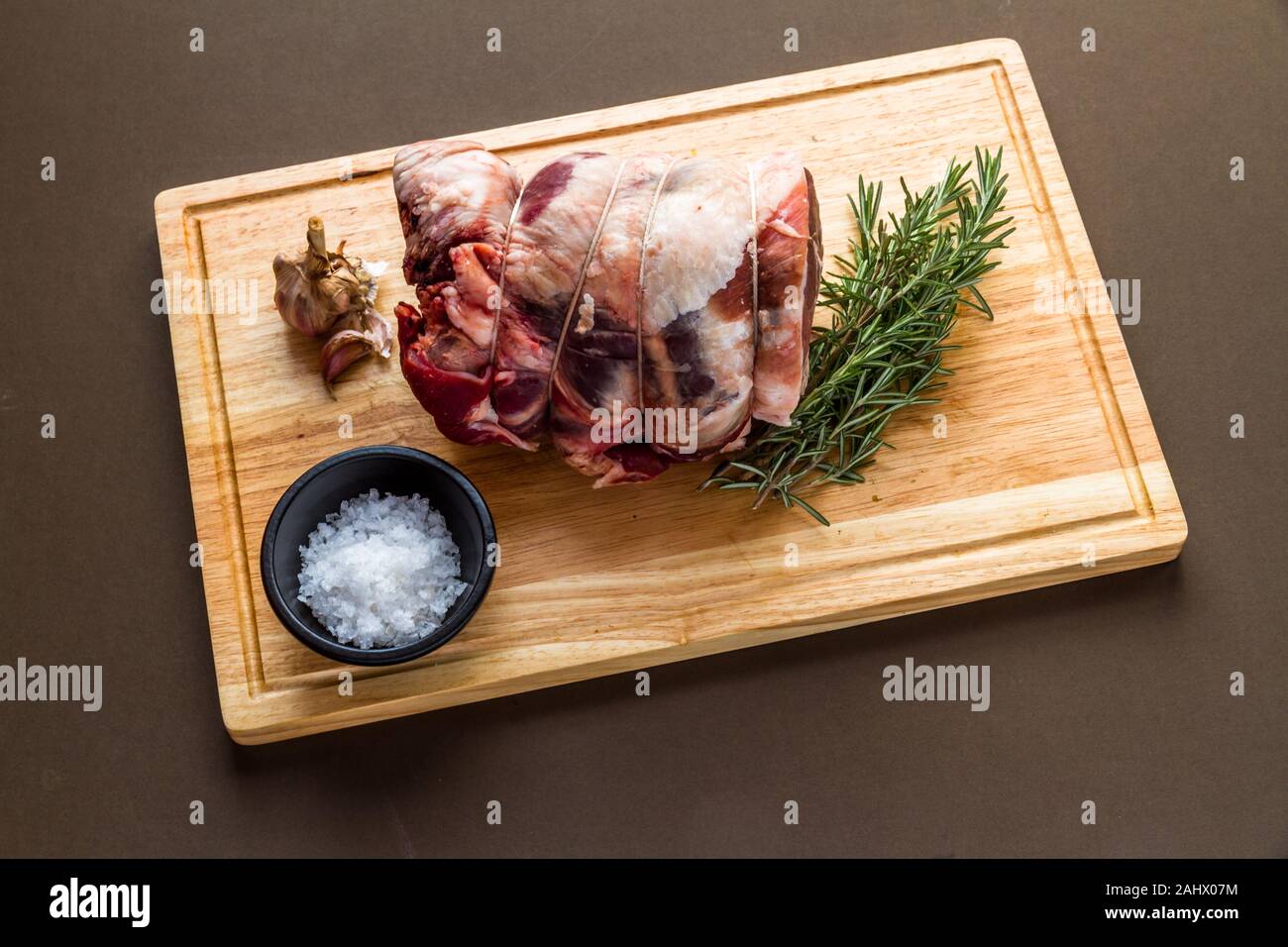 Lake District UK Herdwick crudo di pecora agnello laminato congiunta con i macellai stringa con aglio, rosmarino e sale marino, sul legno tagliere. Foto Stock