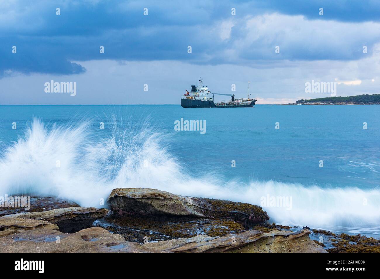 Grande onda colpendo la roccia con intrusione sullo sfondo. Paesaggio marino con nave nautico Foto Stock