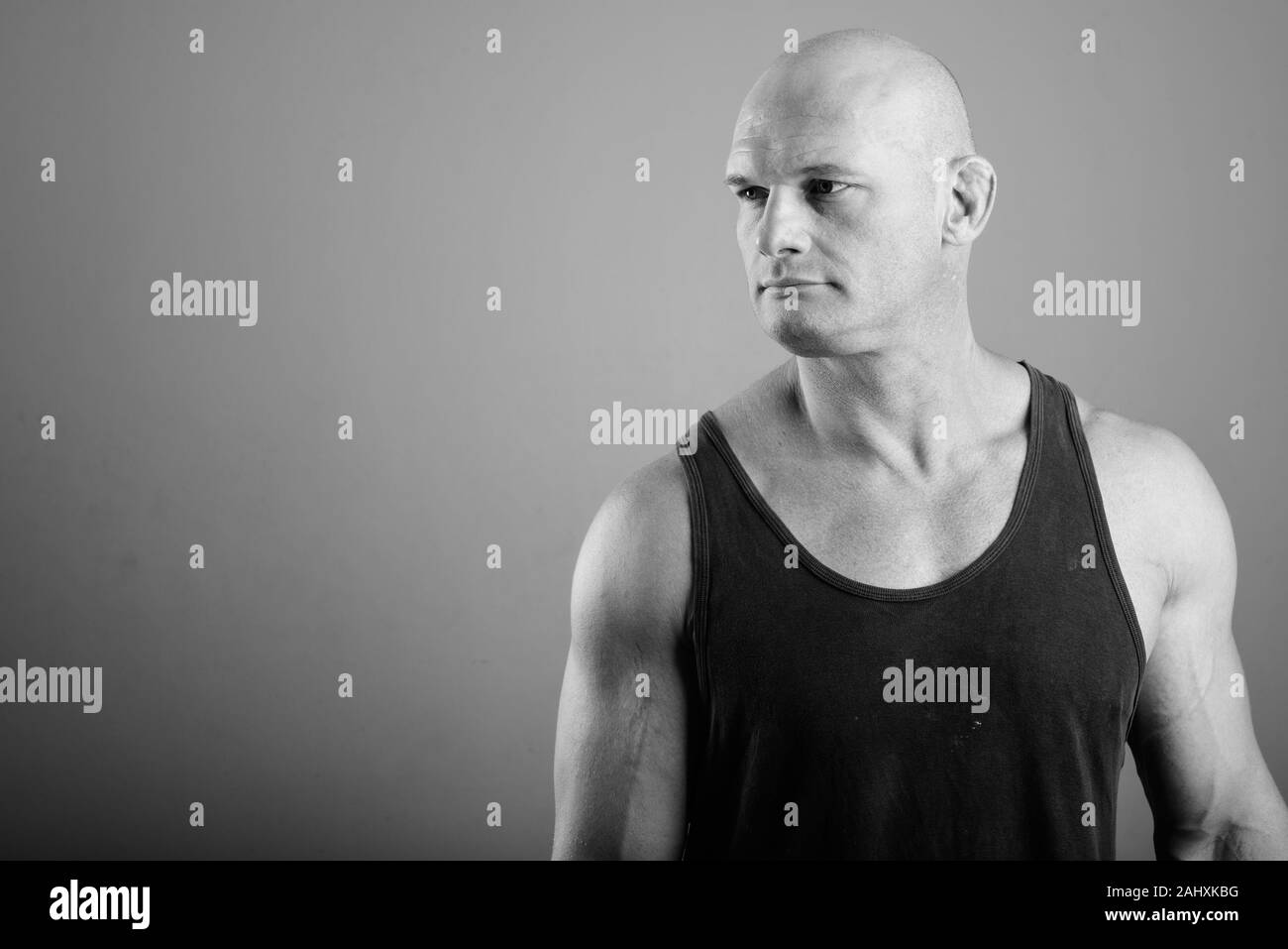 Bald muscolare di uomo che indossa serbatoio superiore contro lo sfondo grigio Foto Stock