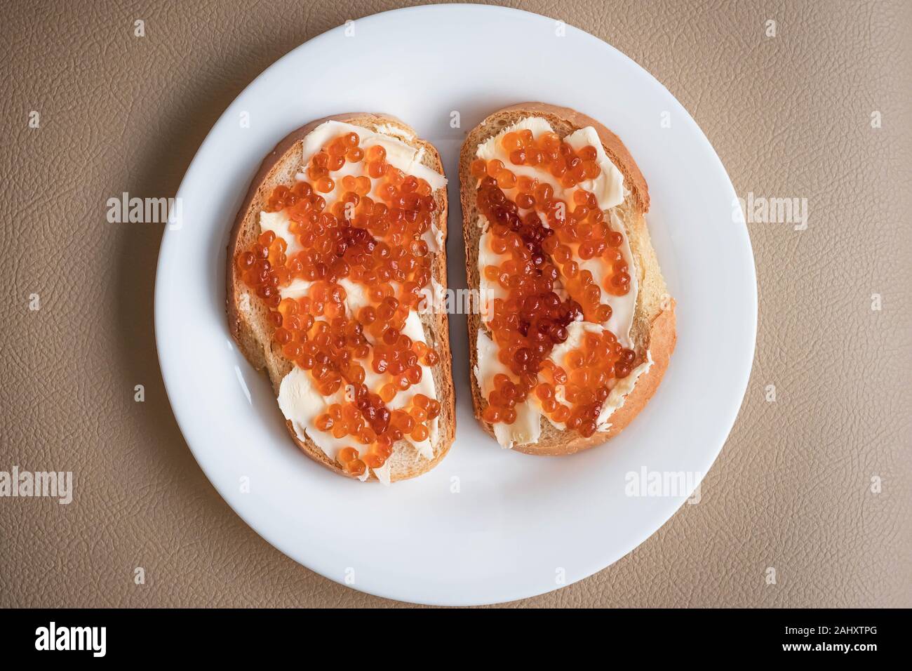 Due panini con burro e caviale rosso su una piastra bianca, vista dall'alto Foto Stock