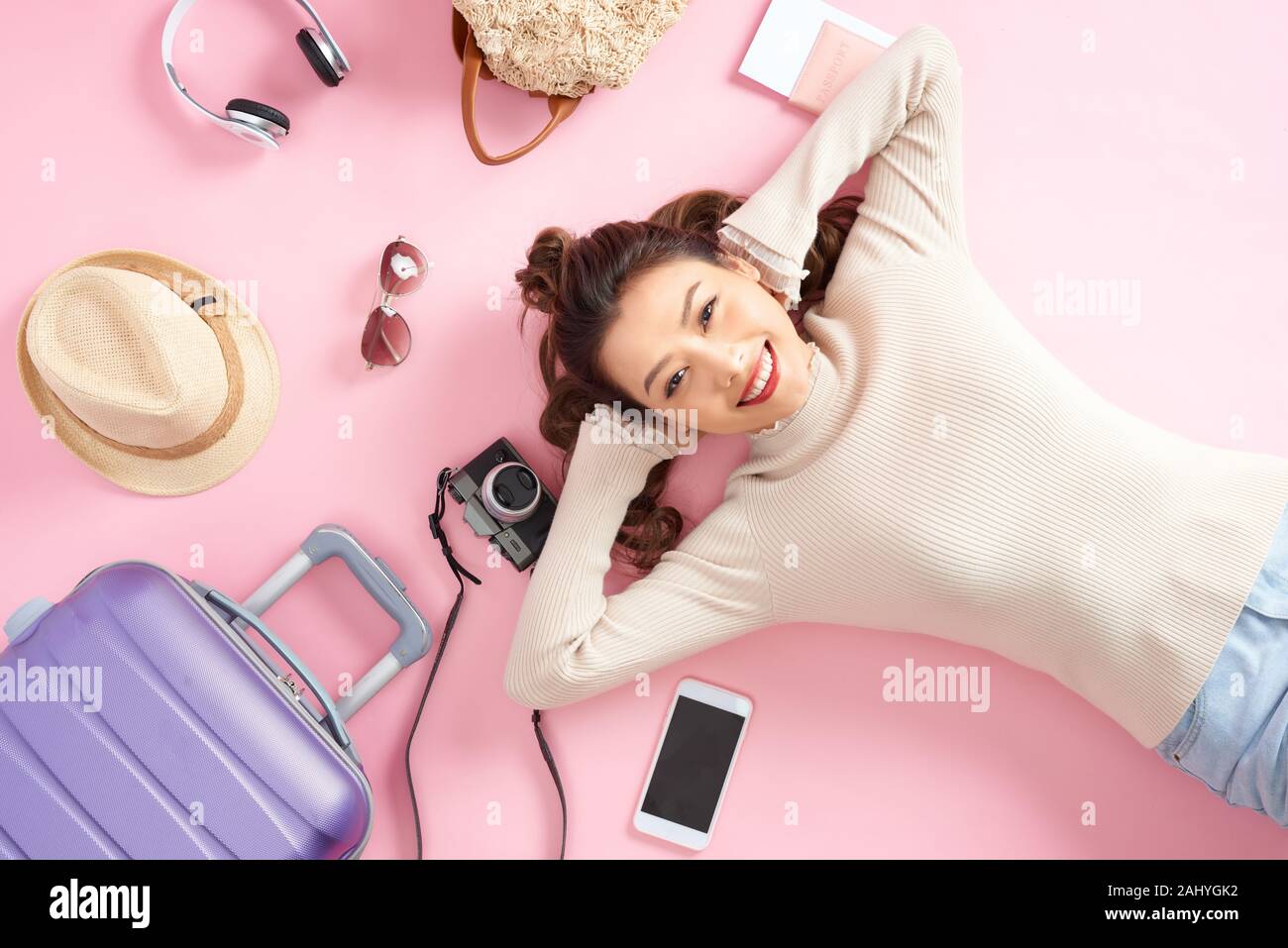 Donna di viaggio sorriso felicemente e cercare da qualche parte giacente sul piano di colore rosa. Vista superiore Foto Stock