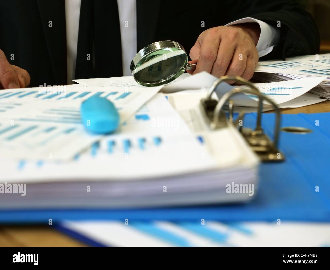 Concetto di audit. Un uomo si siede a un tavolo e controlla i documenti. Pila di carte e di una lente di ingrandimento. Foto Stock