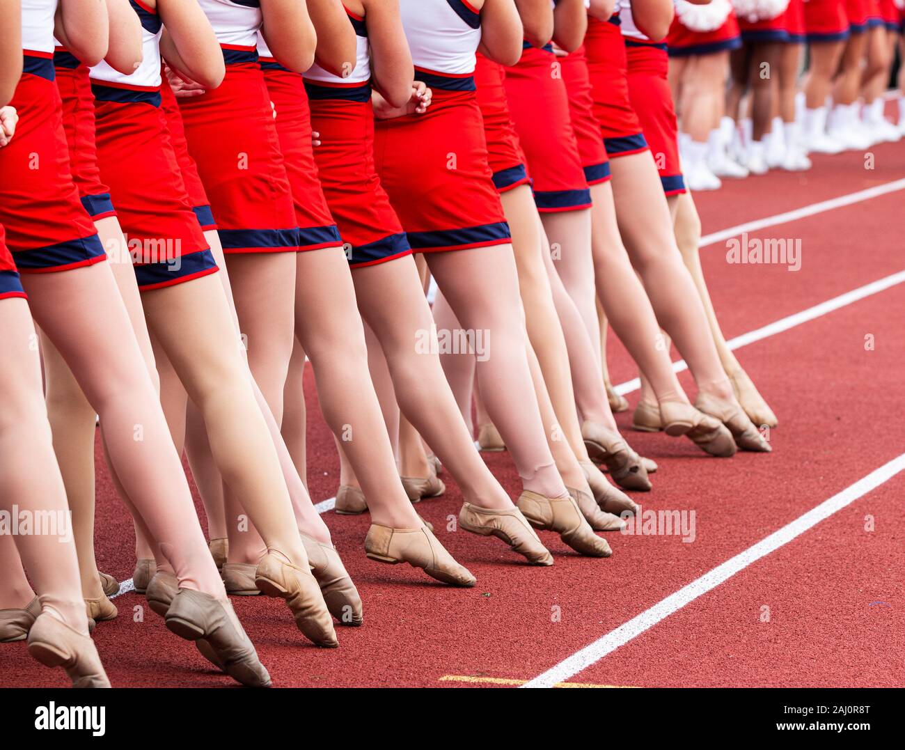 Un liceo squadre kickline gambe con punta appuntita mentre in piedi su una traccia durante l'inno nazionale prima di una partita di calcio. Foto Stock