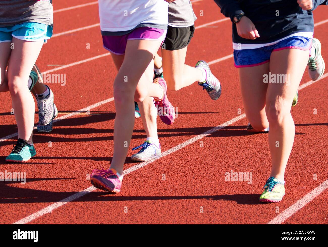 Un gruppo di ragazze su un cross country team non allenamento di velocità su una pista rossa mentre i picchi di usura Foto Stock