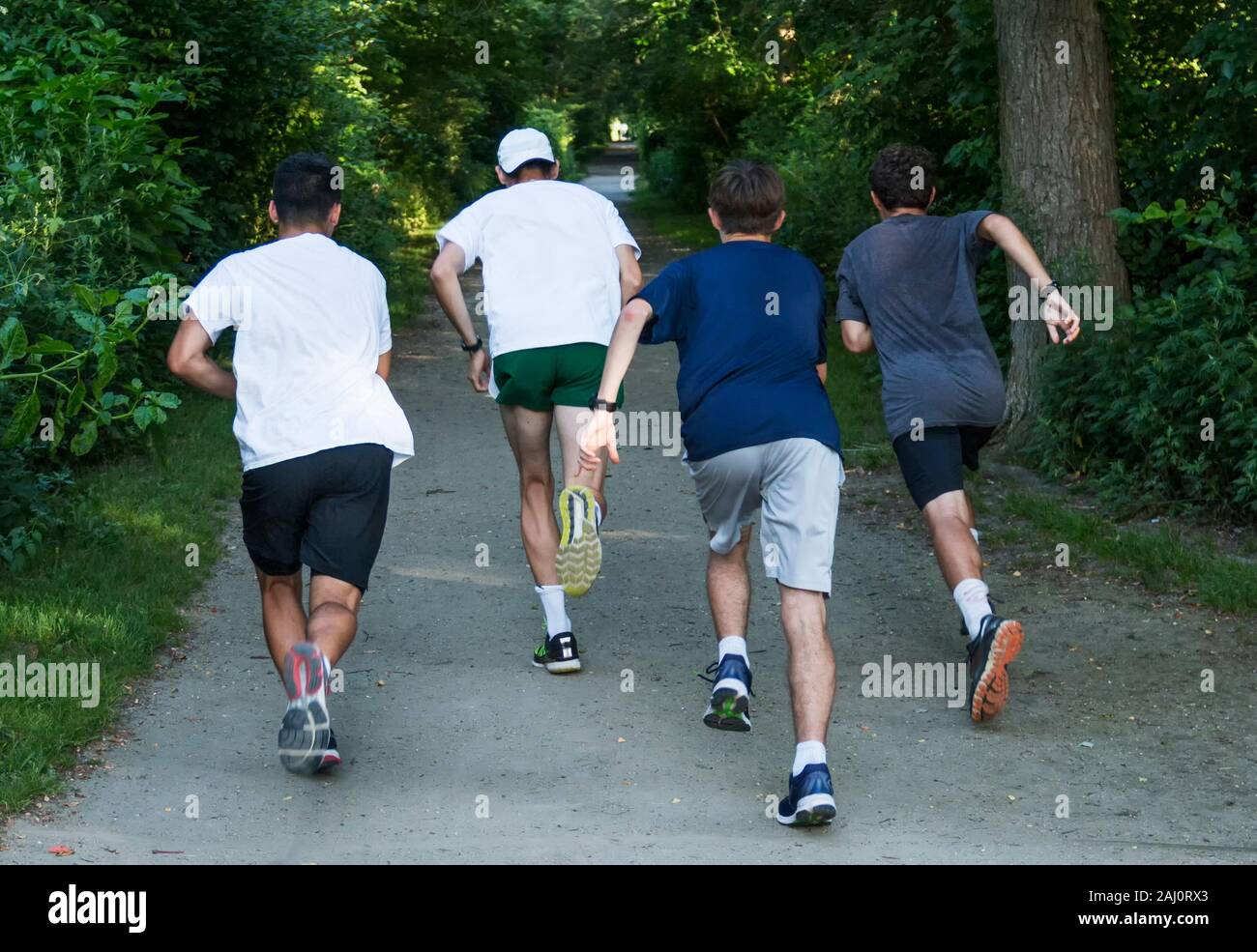 Quattro ragazzi adolescenti stanno iniziando un intervallo corrono verso un viale alberato percorso sporco in un parco locale. Foto Stock