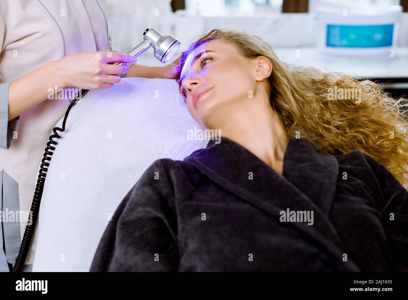 Luce terapia a raggi infrarossi. Testa di Cosmetologia procedura. Close-up di bella donna faccia ricevente a led blu la terapia della luce. Salone estetico dispositivo. Trattamento viso Foto Stock