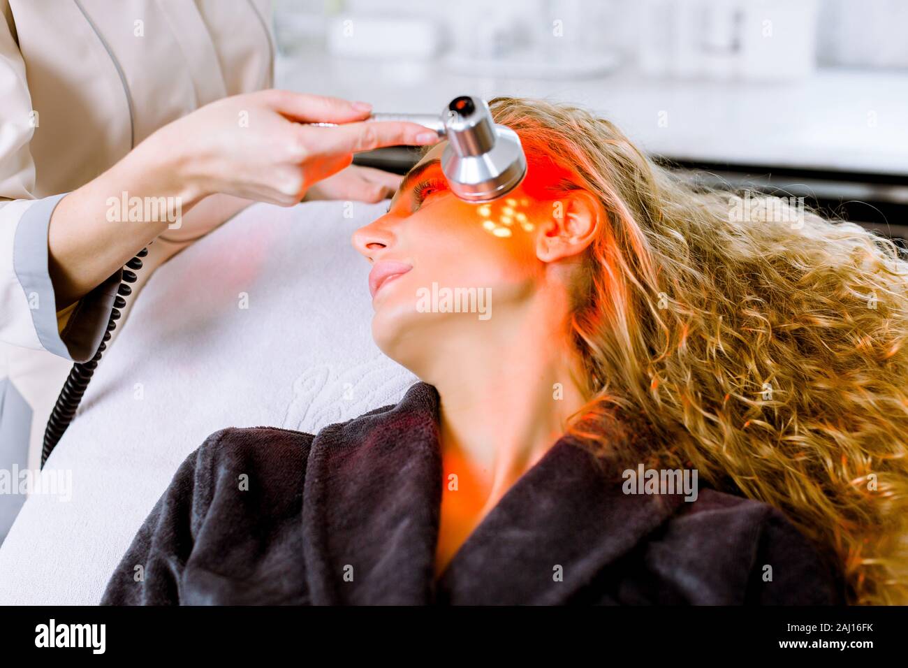 Estetista facendo luce LED rossa terapia per donna bionda in un salone di  bellezza, foto del