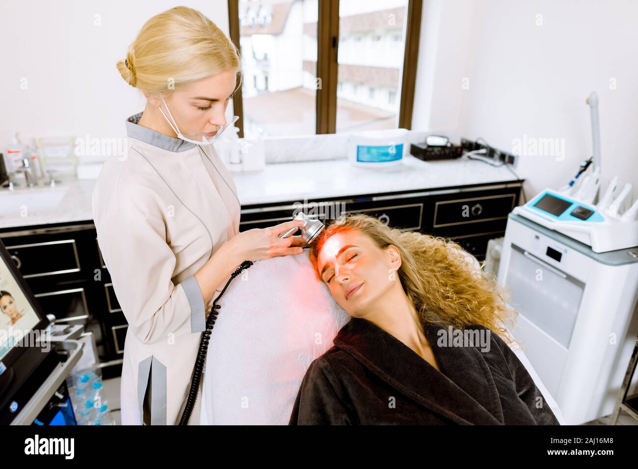 Medico donna conduce la procedura per il ringiovanimento della pelle del viso. Bella donna bionda ricevendo trattamento viso, rimozione di pigmentazione in clinica. Cosm Foto Stock