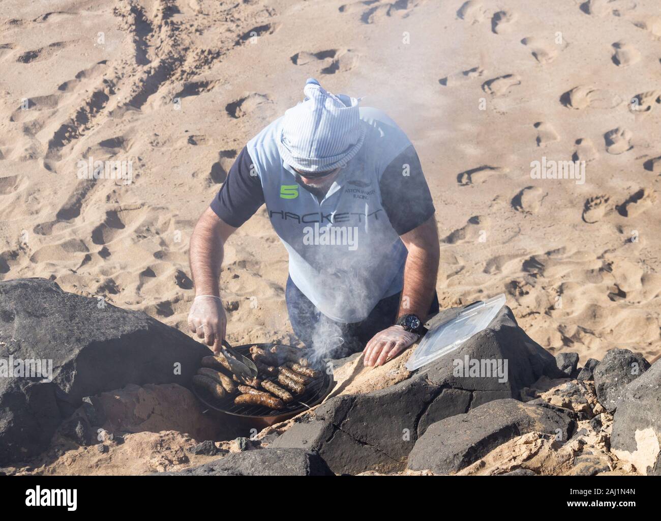L'uomo la cottura di salsicce al barbecue sulla spiaggia, barbecue. Foto Stock