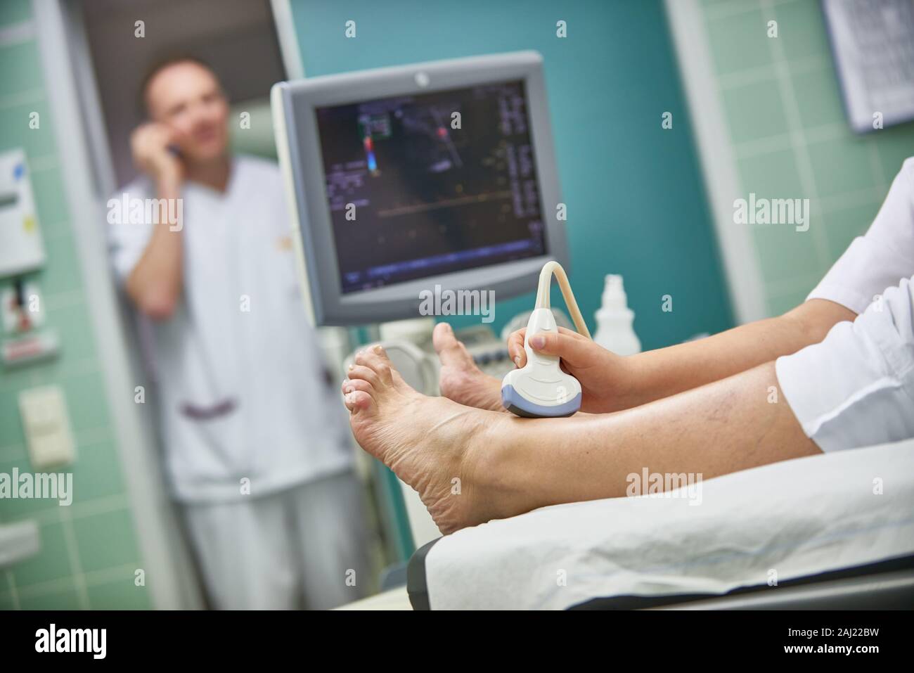 Medico con il dispositivo di ecografia in una mano checkst piede del paziente Foto Stock