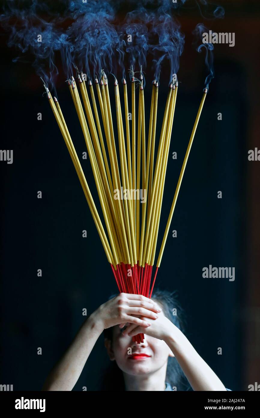 Giovane donna cinese pregando con grande bruciare bastoncini di incenso nelle sue mani, Ah Hoi Chuong Quan Pagoda, Ho Chi Minh City, Vietnam, Indocina, Asia Foto Stock