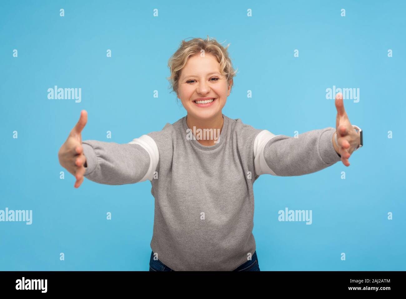 Free Hugs, venite qui! Felice tipo hearted donna con capelli ricci in felpa aprendo le sue mani ampia per dare il benvenuto caloroso e cordiale sorriso ospitale. i Foto Stock