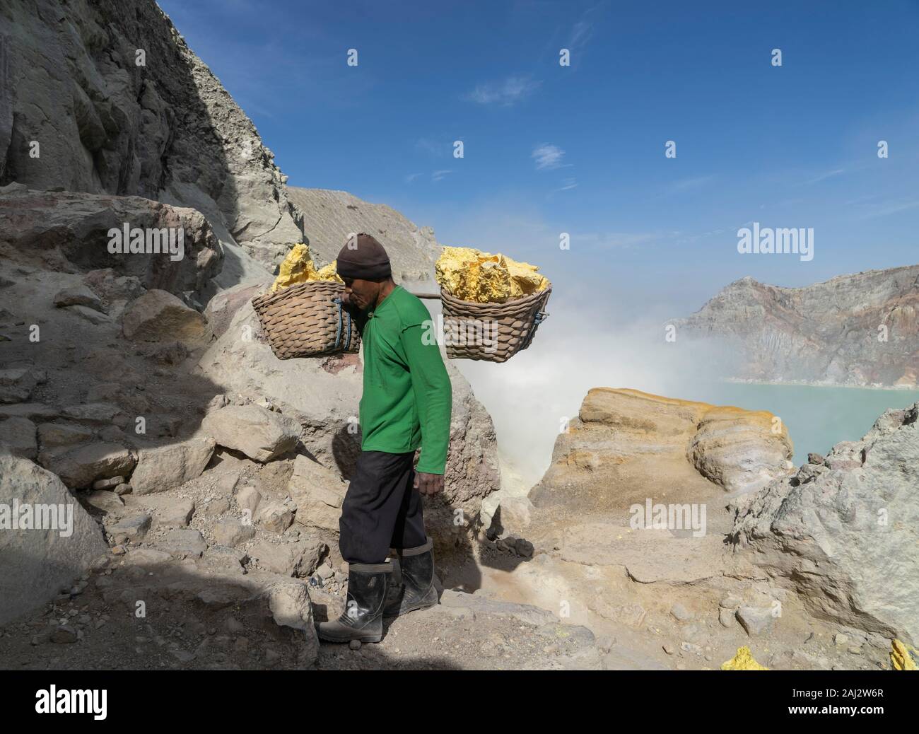 Un minatore trasporta un carico pesante di zolfo navigazione il suo modo fino al cratere del vulcano Ijen.Il vulcano Ijen è uno dei pochi luoghi in cui lo zolfo è ancora minate senza macchine, il cratere di vulcano ha una bocca attiva che produce zolfo elementare. La respirazione nel gas di zolfo può provocare a lungo termine le implicazioni sanitarie ma nonostante ciò non vi è carenza di minatori locali disposti a rischiare tutto per guadagnare un buon stipendio, minatori fare un reddito medio di tre volte superiore al salario locale. Zolfo puro viene utilizzato nella famiglia di prodotti per la pulizia, il make up, esplosivi e purificazione di zucchero. T Foto Stock