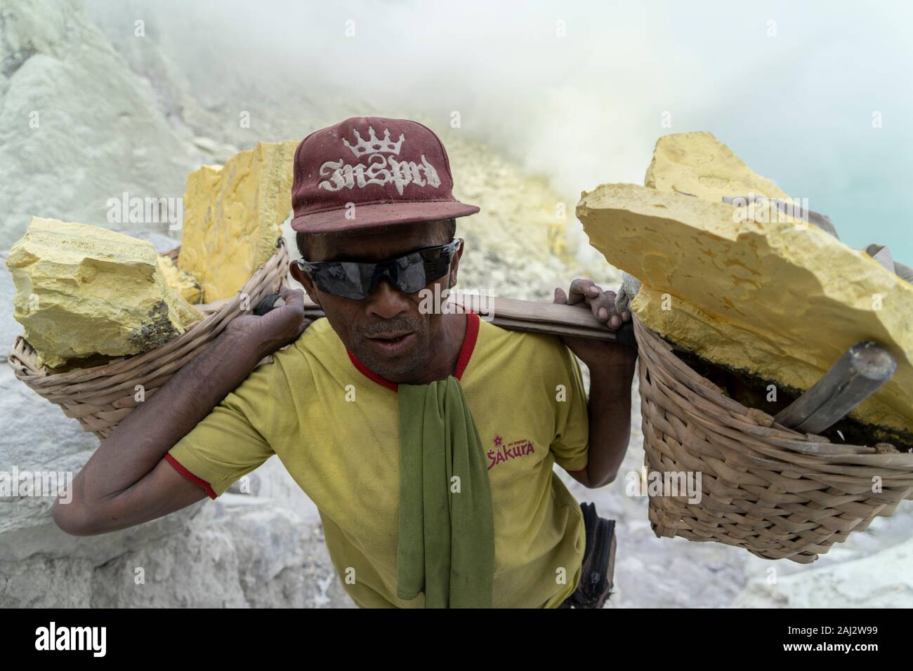 Un indonesiano minatore di zolfo Zolfo portante lungo il difficile percorso fuori del vulcano Ijen.Il vulcano Ijen è uno dei pochi luoghi in cui lo zolfo è ancora minate senza macchine, il cratere di vulcano ha una bocca attiva che produce zolfo elementare. La respirazione nel gas di zolfo può provocare a lungo termine le implicazioni sanitarie ma nonostante ciò non vi è carenza di minatori locali disposti a rischiare tutto per guadagnare un buon stipendio, minatori fare un reddito medio di tre volte superiore al salario locale. Zolfo puro viene utilizzato nella famiglia di prodotti per la pulizia, il make up, esplosivi e purificazione di sug Foto Stock