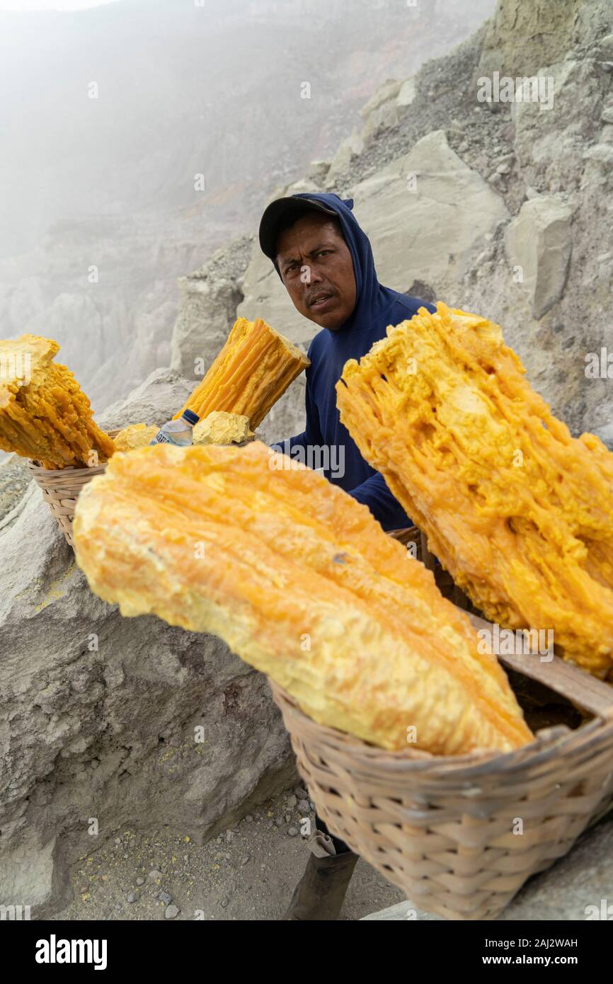 Un indonesiano minatore di zolfo si prende una pausa lungo il difficile percorso fuori del vulcano Ijen.Il vulcano Ijen è uno dei pochi luoghi in cui lo zolfo è ancora minate senza macchine, il cratere di vulcano ha una bocca attiva che produce zolfo elementare. La respirazione nel gas di zolfo può provocare a lungo termine le implicazioni sanitarie ma nonostante ciò non vi è carenza di minatori locali disposti a rischiare tutto per guadagnare un buon stipendio, minatori fare un reddito medio di tre volte superiore al salario locale. Zolfo puro viene utilizzato nella famiglia di prodotti per la pulizia, il make up, esplosivi e purificazione di zucchero. Foto Stock
