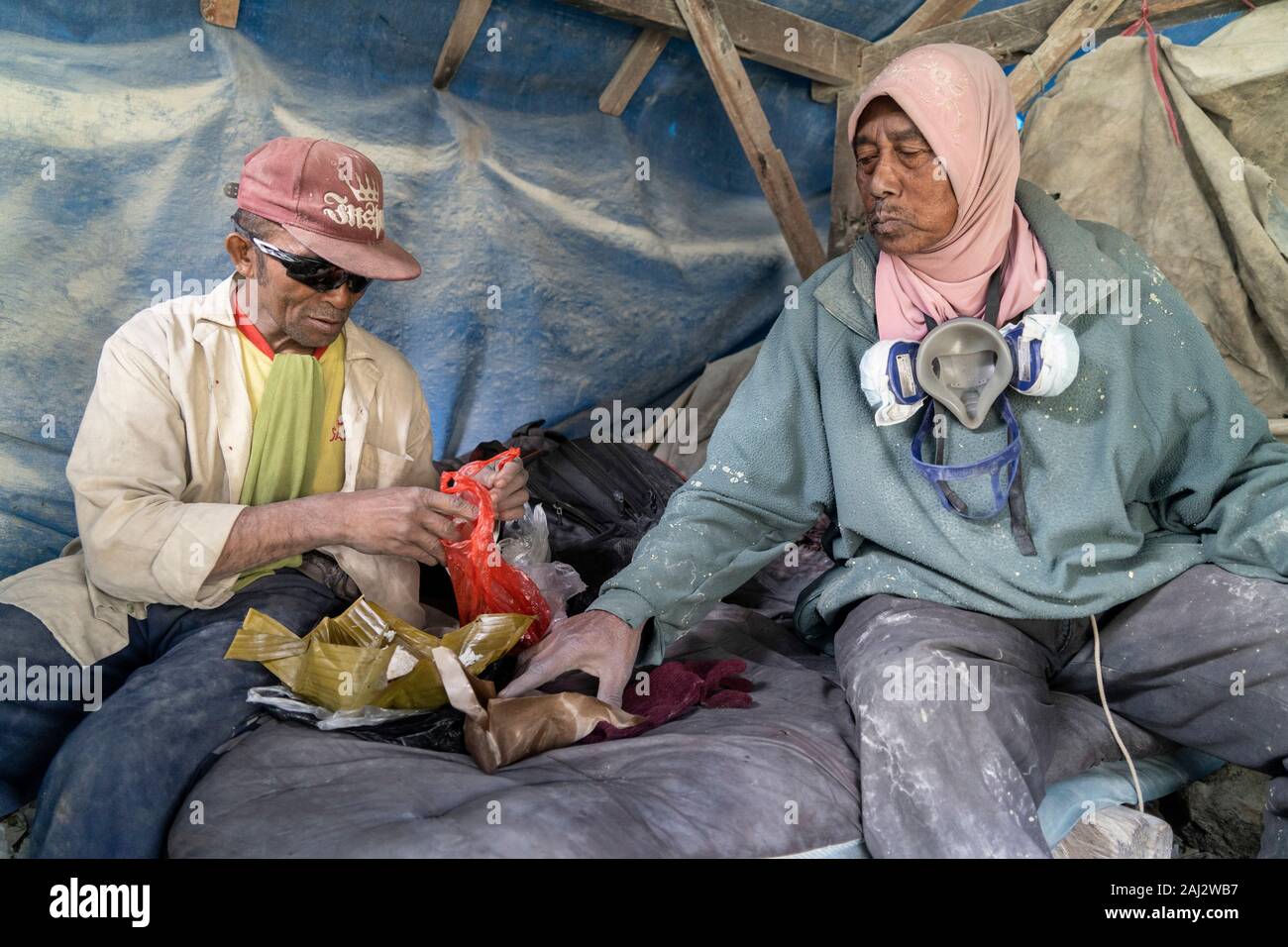 Due minatori di zolfo prendere una pausa pranzo in rifugio profondo dentro il vulcano Ijen.Il vulcano Ijen è uno dei pochi luoghi in cui lo zolfo è ancora minate senza macchine, il cratere di vulcano ha una bocca attiva che produce zolfo elementare. La respirazione nel gas di zolfo può provocare a lungo termine le implicazioni sanitarie ma nonostante ciò non vi è carenza di minatori locali disposti a rischiare tutto per guadagnare un buon stipendio, minatori fare un reddito medio di tre volte superiore al salario locale. Zolfo puro viene utilizzato nella famiglia di prodotti per la pulizia, il make up, esplosivi e purificazione di zucchero. Il vulcano als Foto Stock