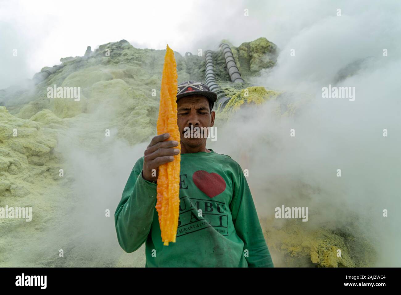 Un minatore indonesiano con un grande pezzo di zolfo da miniera il vulcano Ijen.Il vulcano Ijen è uno dei pochi luoghi in cui lo zolfo è ancora minate senza macchine, il cratere di vulcano ha una bocca attiva che produce zolfo elementare. La respirazione nel gas di zolfo può provocare a lungo termine le implicazioni sanitarie ma nonostante ciò non vi è carenza di minatori locali disposti a rischiare tutto per guadagnare un buon stipendio, minatori fare un reddito medio di tre volte superiore al salario locale. Zolfo puro viene utilizzato nella famiglia di prodotti per la pulizia, il make up, esplosivi e purificazione di zucchero. Il vol Foto Stock