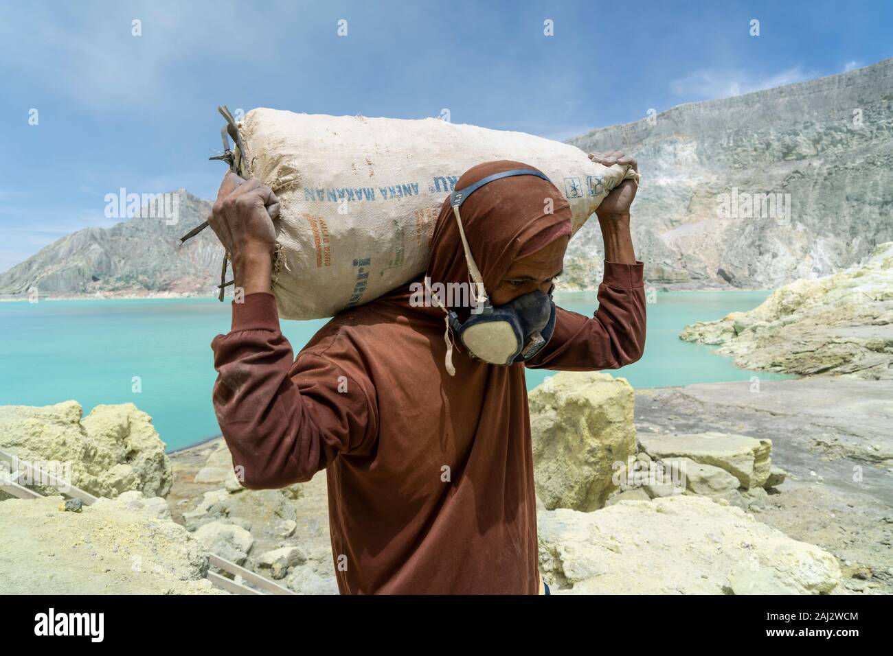 Un minatore indonesiano passeggiate oltre il lago tossico carico di zolfo in un sacco di profondità dentro il vulcano Ijen.Il vulcano Ijen è uno dei pochi luoghi in cui lo zolfo è ancora minate senza macchine, il cratere di vulcano ha una bocca attiva che produce zolfo elementare. La respirazione nel gas di zolfo può provocare a lungo termine le implicazioni sanitarie ma nonostante ciò non vi è carenza di minatori locali disposti a rischiare tutto per guadagnare un buon stipendio, minatori fare un reddito medio di tre volte superiore al salario locale. Zolfo puro viene utilizzato nella famiglia di prodotti per la pulizia, il make up, esplosivi e purificazione Foto Stock
