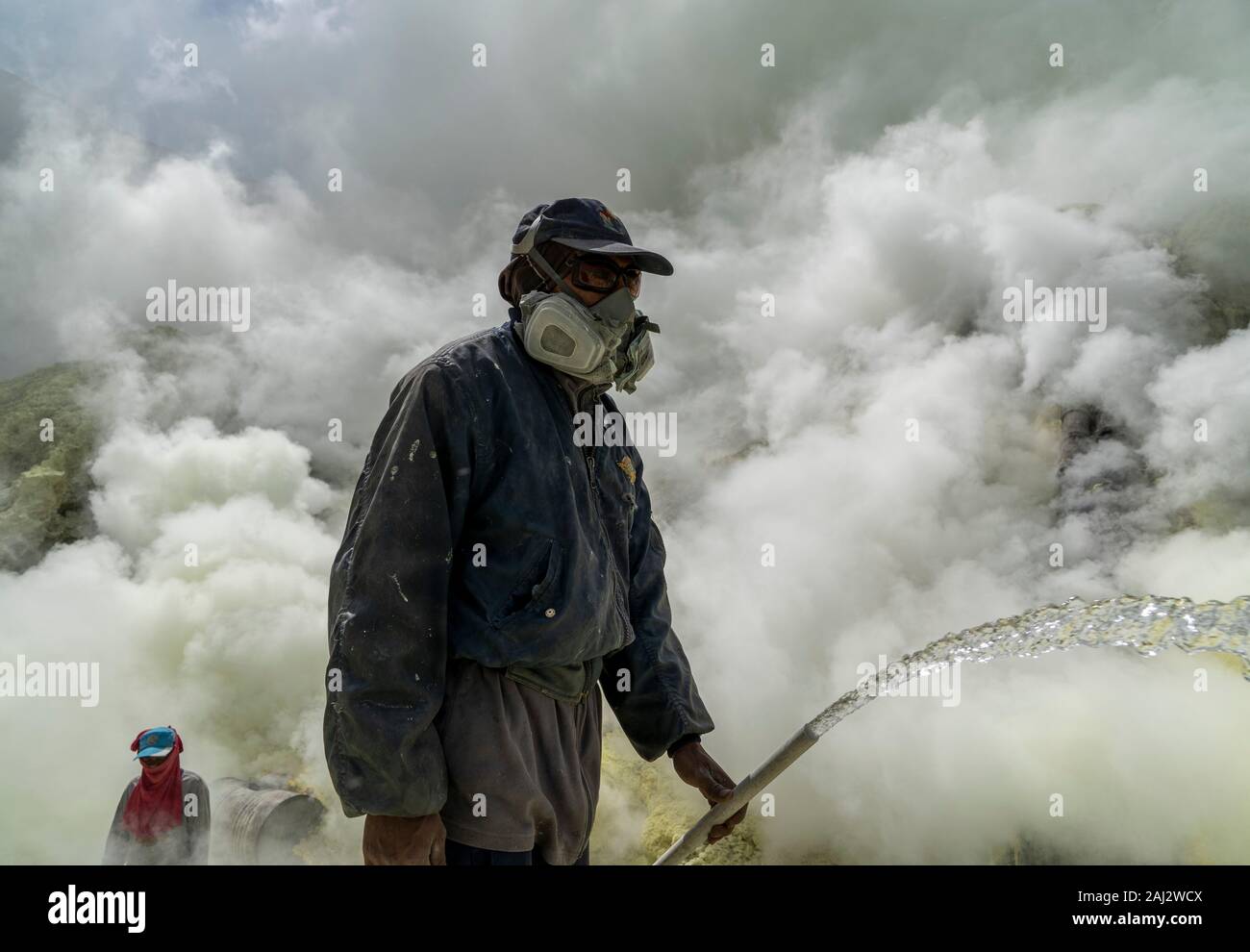 Un minatore indonesiano spruzza i tubi in acciaio con acqua per raffreddarli al vulcano Ijen.Il vulcano Ijen è uno dei pochi luoghi in cui lo zolfo è ancora minate senza macchine, il cratere di vulcano ha una bocca attiva che produce zolfo elementare. La respirazione nel gas di zolfo può provocare a lungo termine le implicazioni sanitarie ma nonostante ciò non vi è carenza di minatori locali disposti a rischiare tutto per guadagnare un buon stipendio, minatori fare un reddito medio di tre volte superiore al salario locale. Zolfo puro viene utilizzato nella famiglia di prodotti per la pulizia, il make up, esplosivi e purificazione di zucchero. Foto Stock