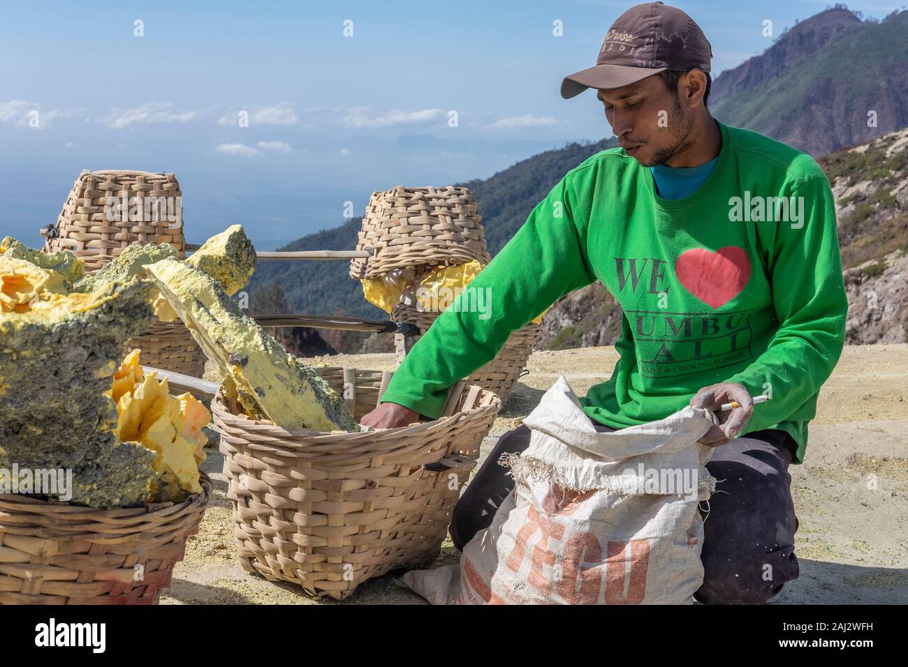 Un Indonesia minatore di zolfo si rompe il suo carico di zolfo in piccoli pezzi prima che egli trasporta verso il basso il vulcano Ijen.Il vulcano Ijen è uno dei pochi luoghi in cui lo zolfo è ancora minate senza macchine, il cratere di vulcano ha una bocca attiva che produce zolfo elementare. La respirazione nel gas di zolfo può provocare a lungo termine le implicazioni sanitarie ma nonostante ciò non vi è carenza di minatori locali disposti a rischiare tutto per guadagnare un buon stipendio, minatori fare un reddito medio di tre volte superiore al salario locale. Zolfo puro viene utilizzato nella famiglia di prodotti per la pulizia, il make up, explos Foto Stock