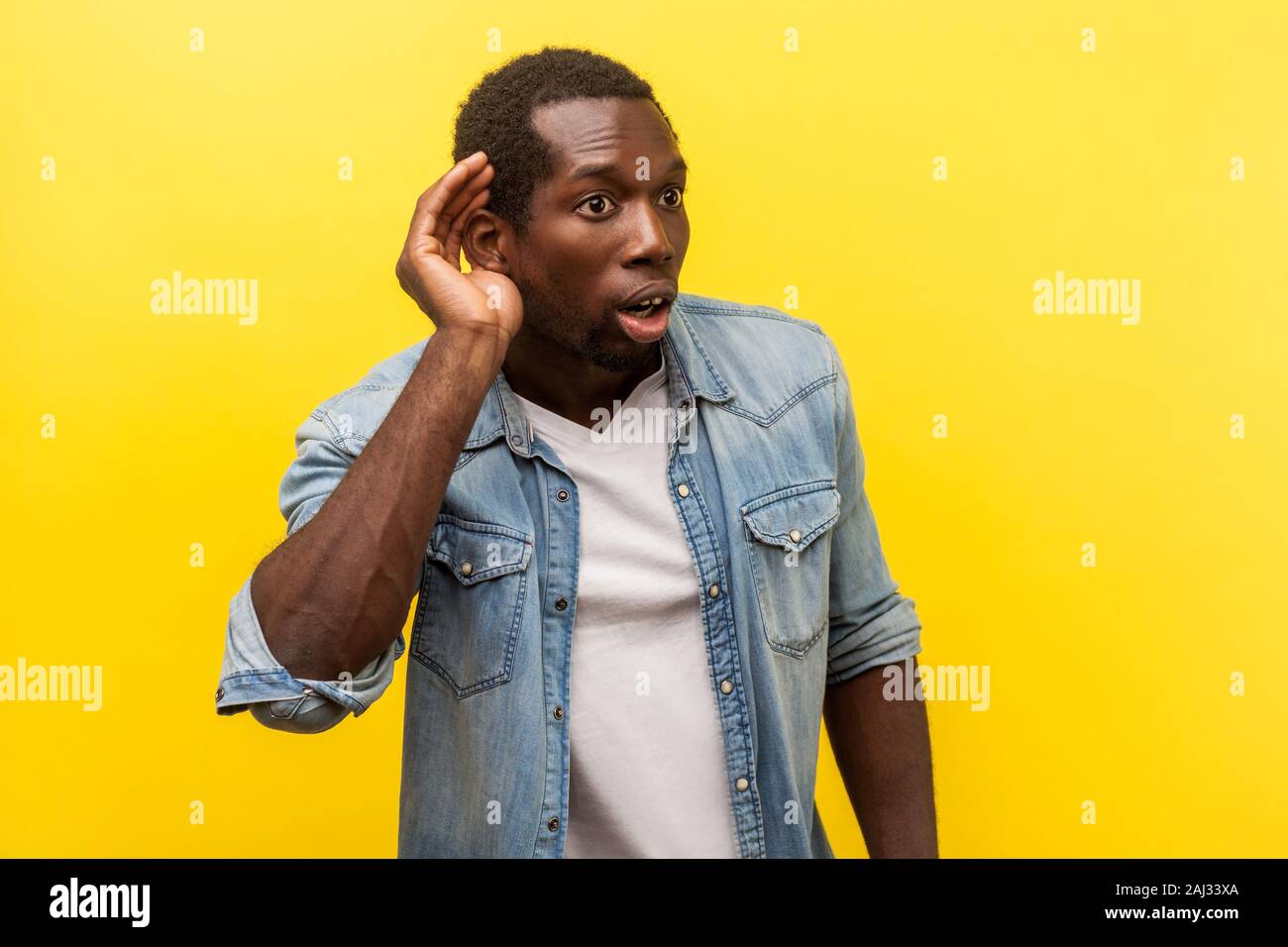 Ritratto di attenta sorpreso uomo in denim Camicia casual con arrotolato manicotti a mettere mano all'orecchio per ascoltare meglio, ascoltando con attenzione le voci. Foto Stock