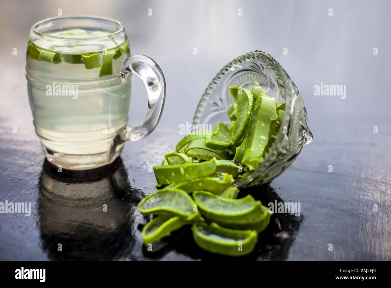 In prossimità della tazza di vetro su una superficie di legno contenenti aloe vera detox drink nel lungo con il suo intero ingredienti grezzi con esso. Inquadratura orizzontale con blurre Foto Stock