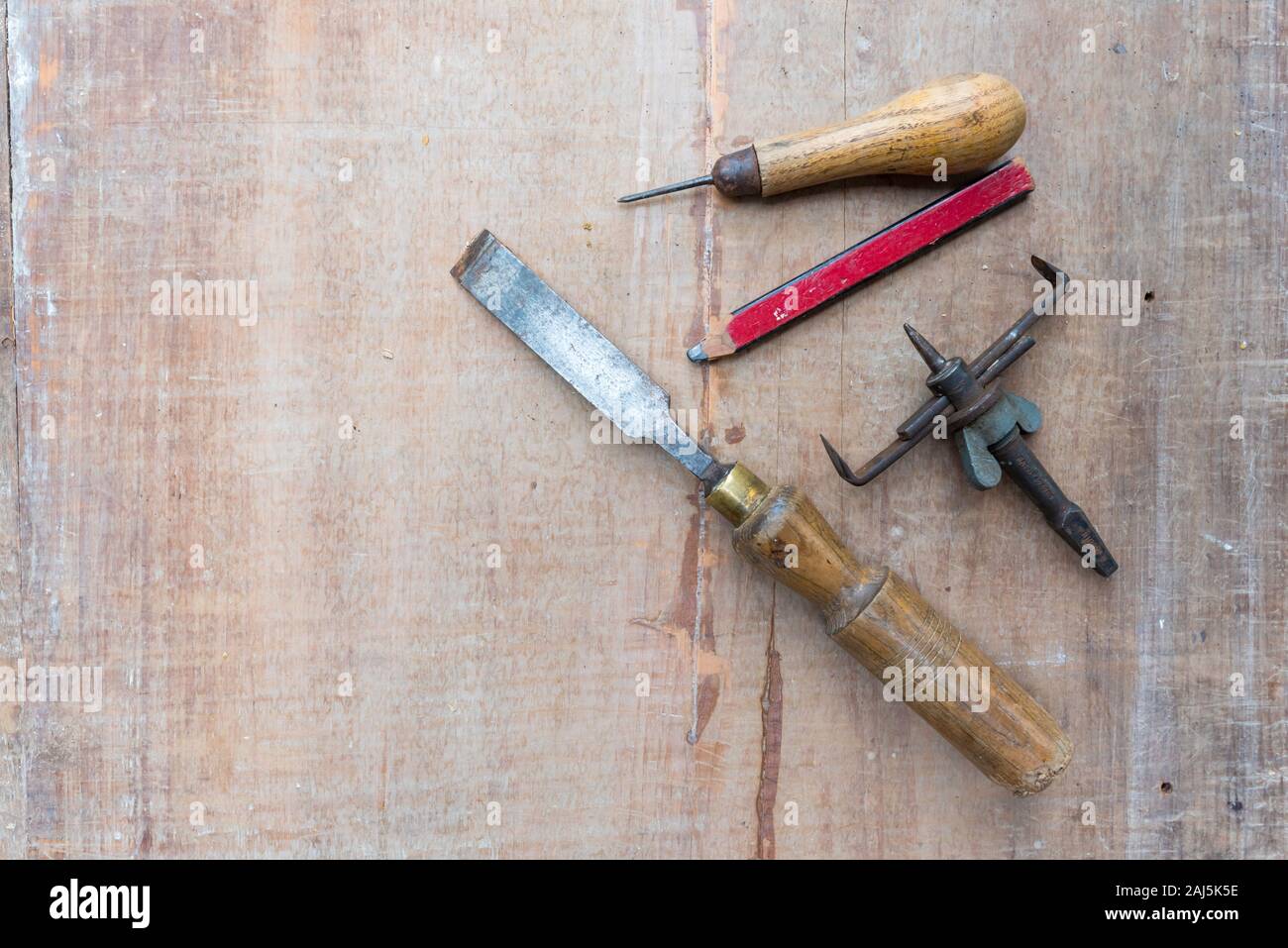 Un vecchio scalpello ed altri utensili a mano che giace piatto su una superficie ruvida pezzo di legname con contrassegni di vernice e graffi Foto Stock