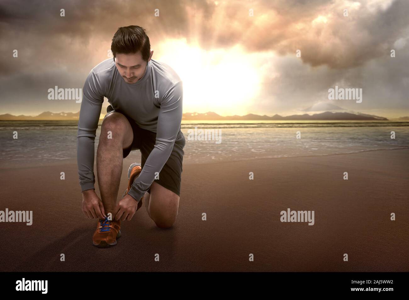 Asian runner uomo in esecuzione di legatura lacci delle scarpe sulla spiaggia con la luce del sole sullo sfondo Foto Stock