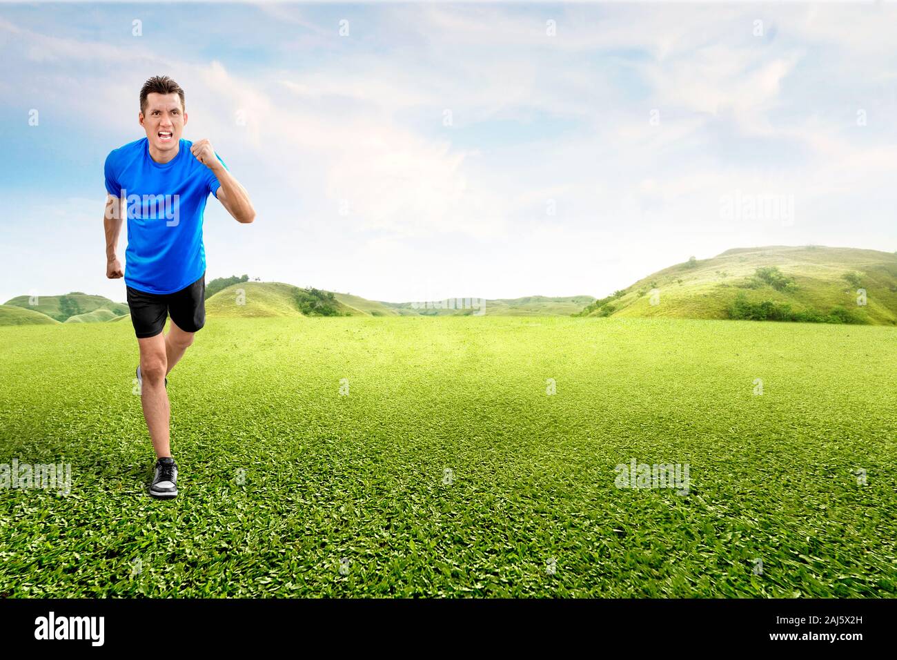Asian runner uomo in esecuzione sul campo verde con un cielo blu sullo sfondo Foto Stock