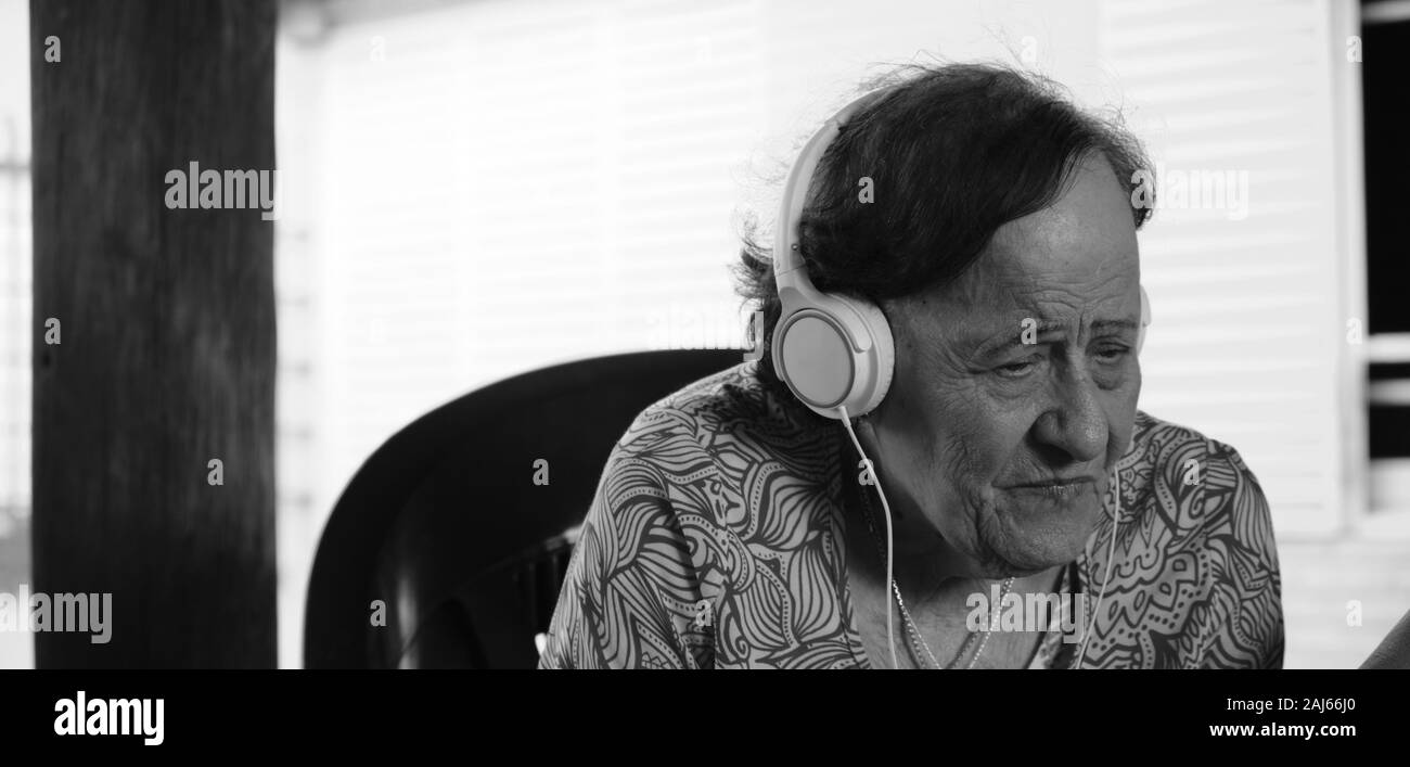 Un ritratto di una donna anziana in ascolto e ascolto di musica con cuffie per esterni Foto Stock