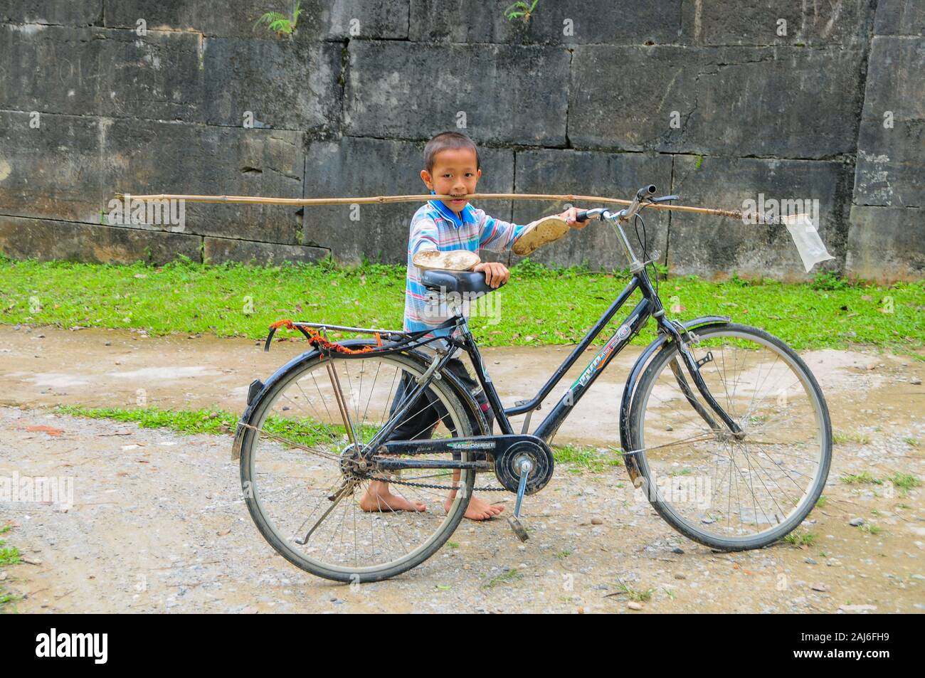 Ho Cittadella, Vietnam; 9 maggio 2014. Giovane ragazzo in bicicletta di spinta e portante una farfalla che cattura net nella sua bocca. Foto Stock