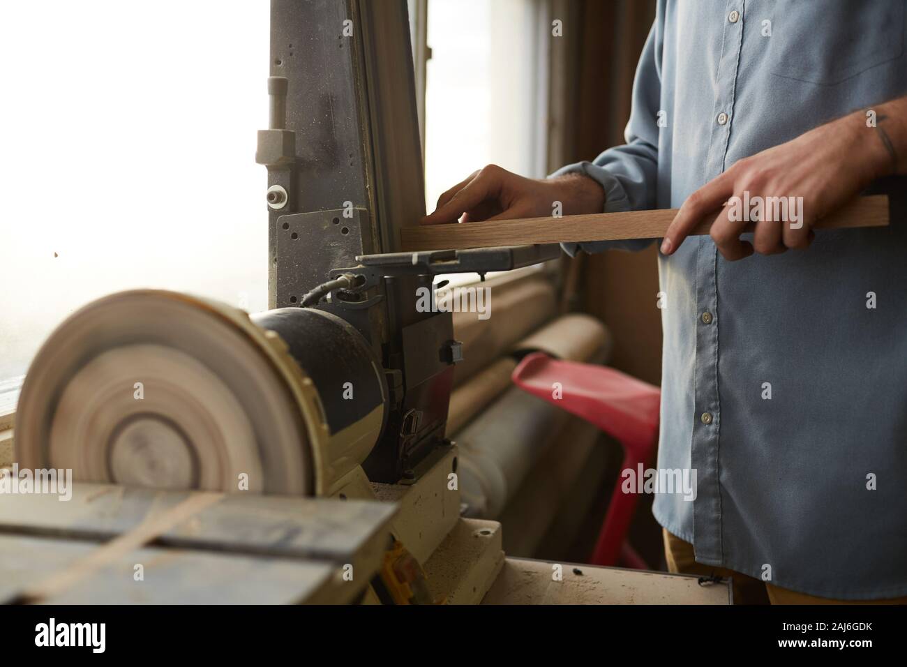 Close-up del giovane lavoratore manuale azienda tavolato in legno e la macinazione mediante tornio in officina Foto Stock