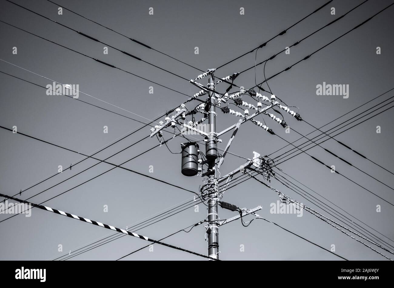 Fili alta tensione multi direzione sul polo elettrico con trasformatore contro il luminoso cielo blu Foto Stock