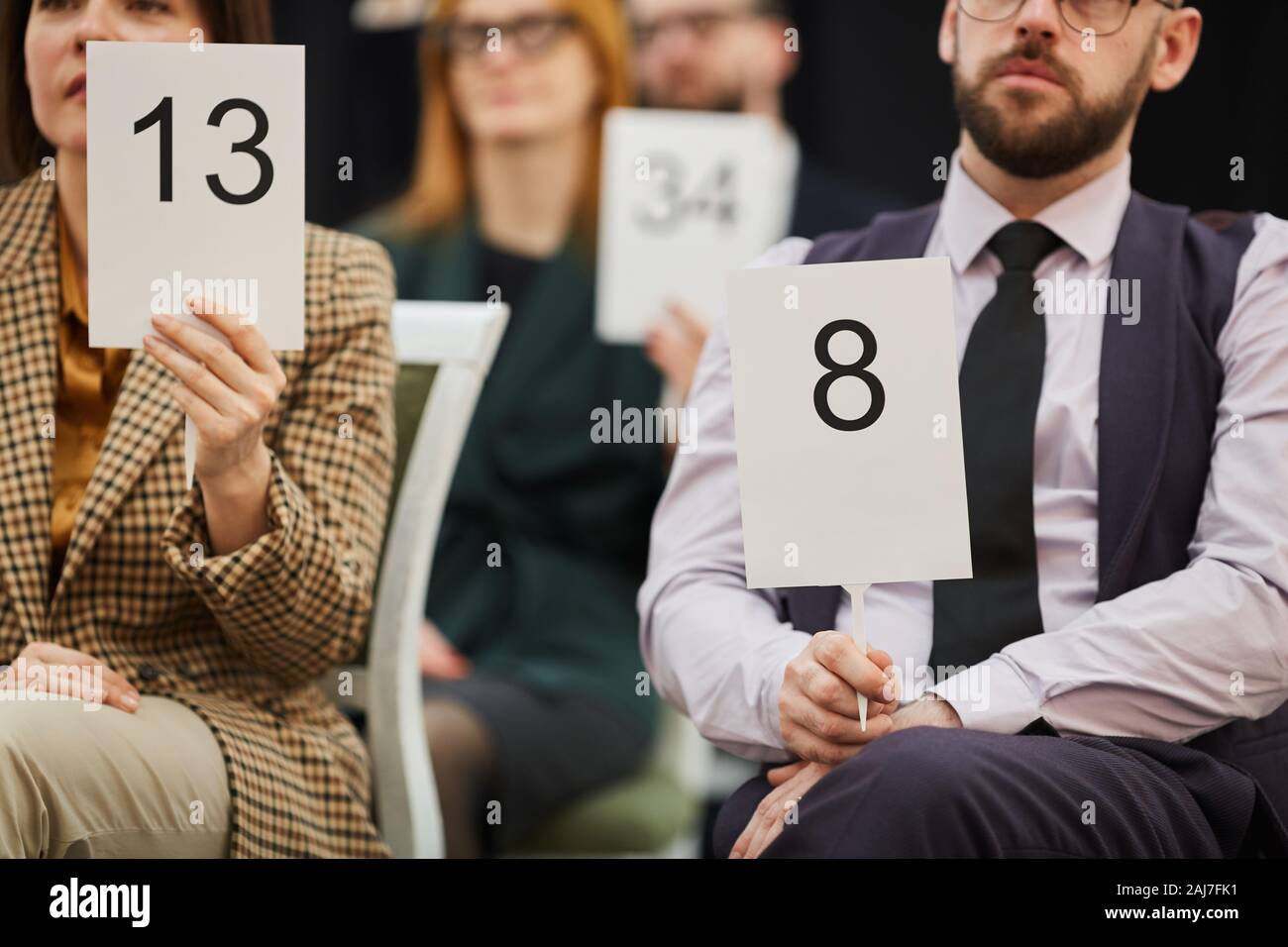 Un gruppo di persone di affari tenendo i segni con i numeri mentre essi seduti su asta Foto Stock