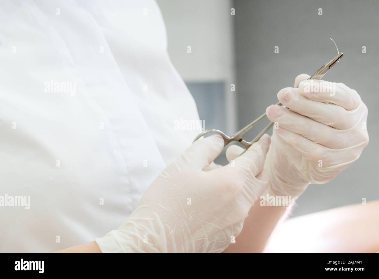 Medico con una pinza chirurgica tenendo un ago di sutura Foto Stock