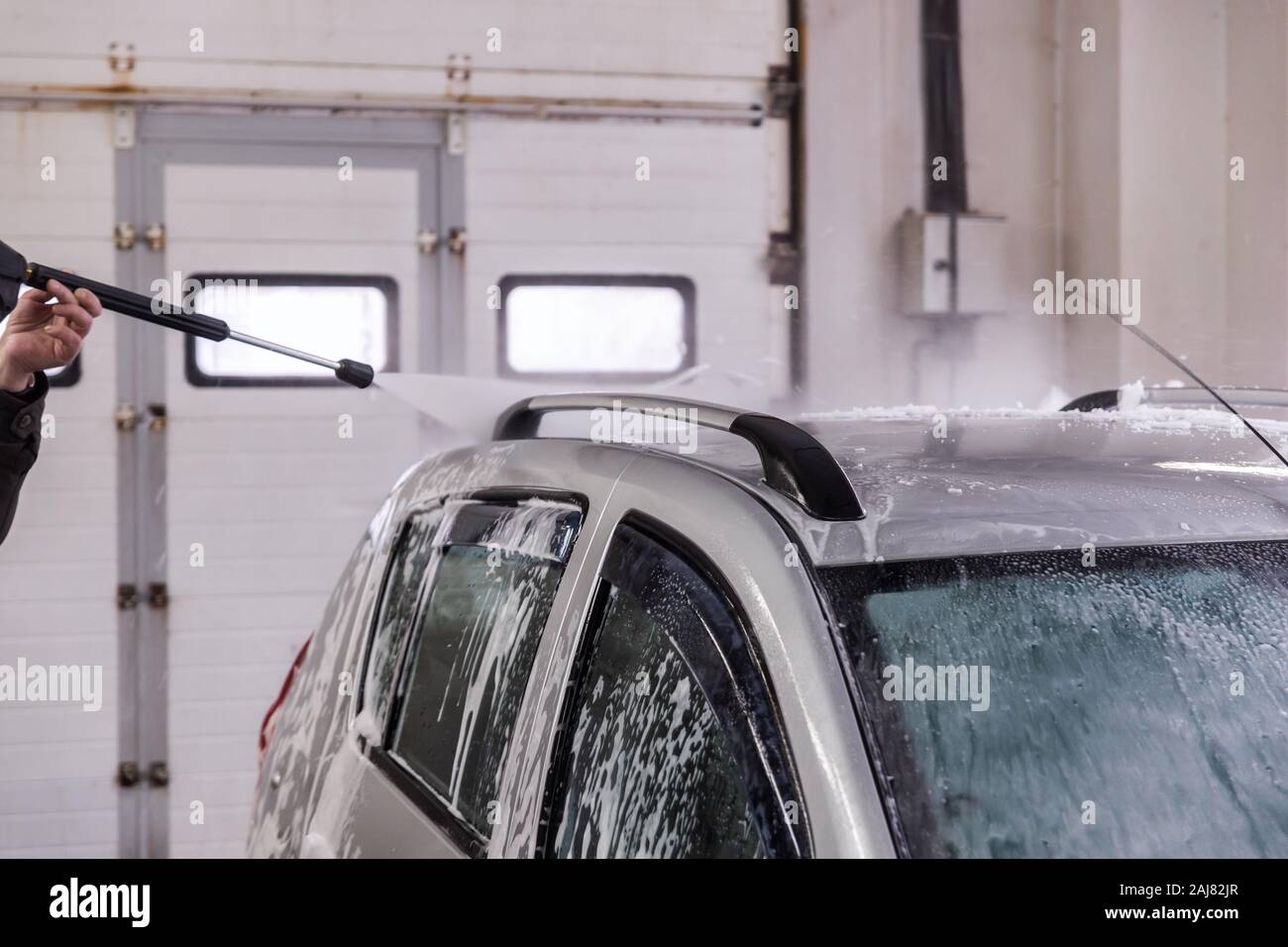 Piscina auto lavaggio auto. Processo di rimozione di schiuma di sapone dal tetto del veicolo con acqua ad alta pressione - flusso di close-up vith messa a fuoco selettiva e motion Foto Stock