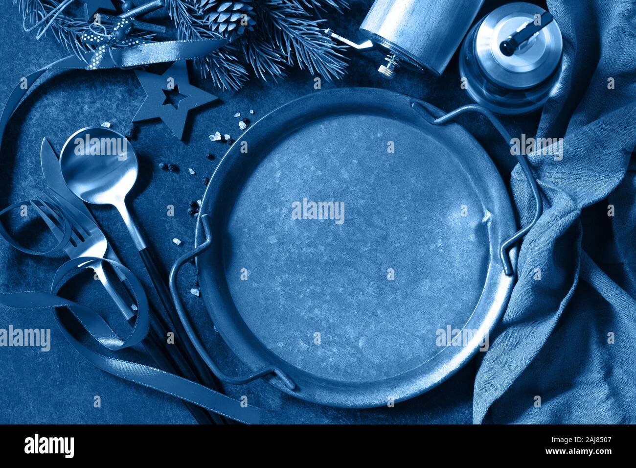 Blu classico 2020. La sfumatura del colore tavolozza. Cena di Natale concetto, sfondo culinario. Una piastra di metallo, posate e tovagliolo su ripiani di pietra. Tabella Foto Stock